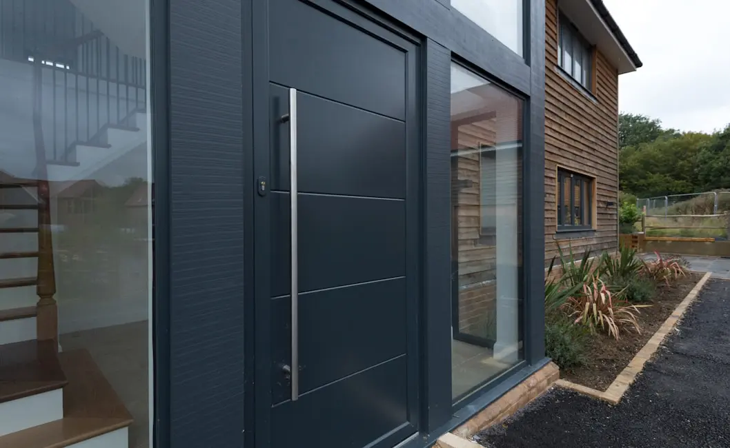 Anthracite Origin front door with a long pull bar and glazed side panel beside timber cladding