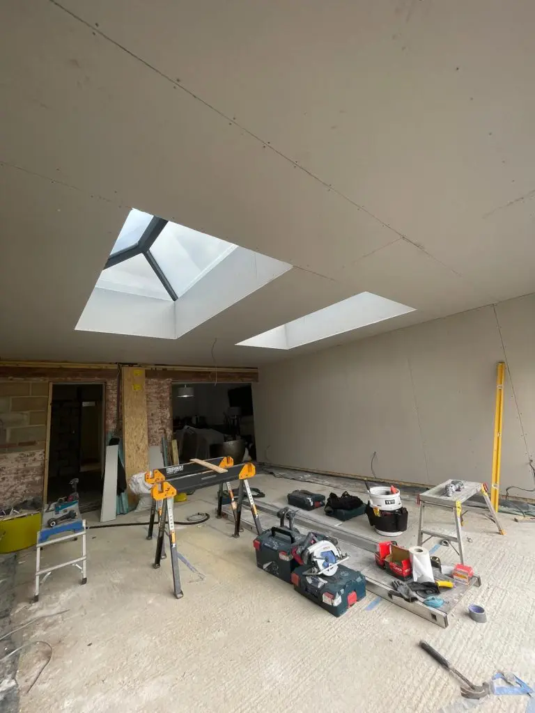 Plasterboarded interior of the Wix, Manningtree extension showing twin roof lanterns, the opening to the house and tools during construction.