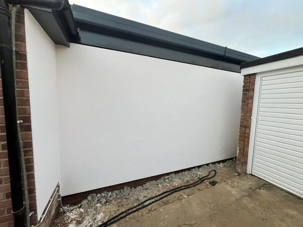 White rendered side wall of the Wix, Manningtree extension beneath grey roof fascia and guttering, beside the garage.